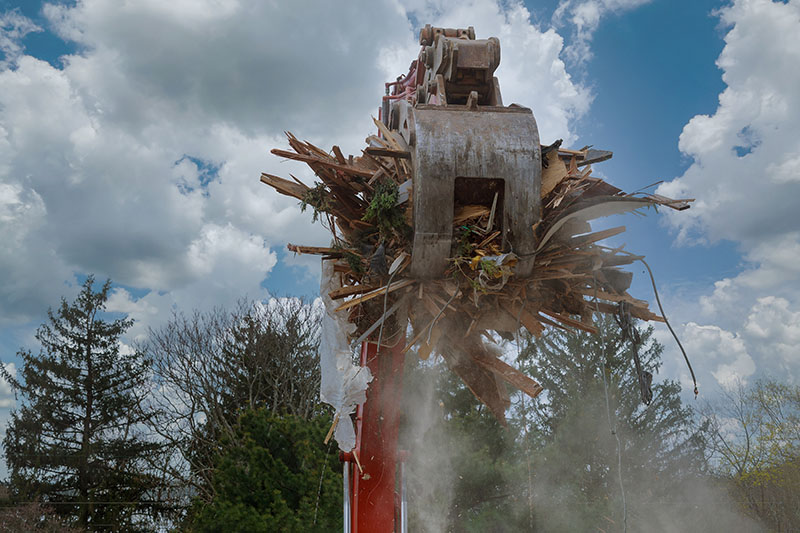 Excavator claw operated by a demolition company lifting debris from a demolished wooden structure.
